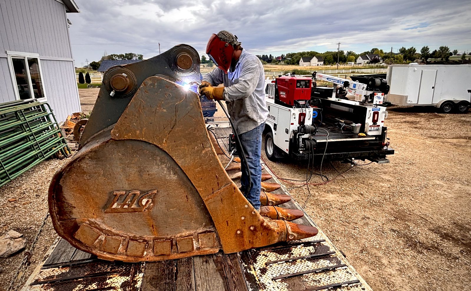 Idaho Welding Services welder repairing a cracked excavator bucket on a trailer in the Treasure Valley